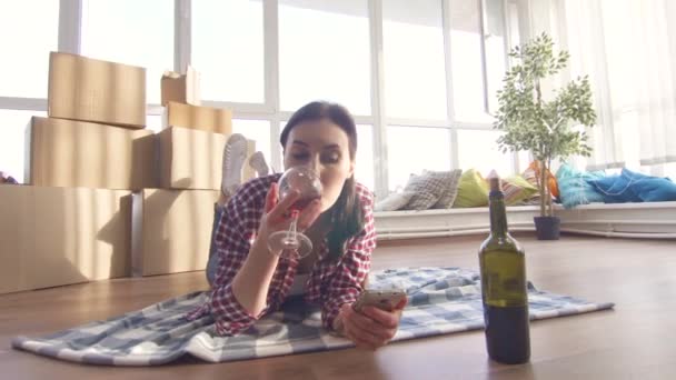 Chica solitaria tumbada en el suelo bebiendo vino y usando un teléfono inteligente — Vídeo de stock