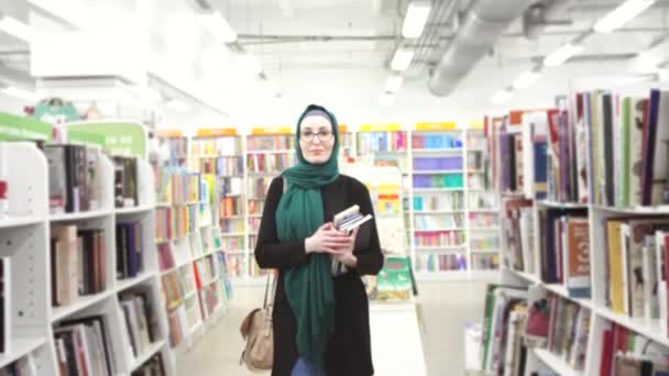 Красивая девушка в хиджабе с книгами в руках в книжном магазине — стоковое видео