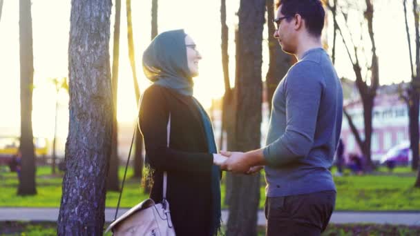Мужчина и женщина в хиджабе держатся за руки в парке — стоковое видео