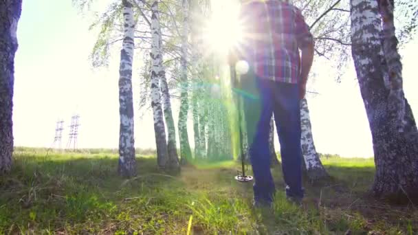 Un hombre con un detector de metales camina por el bosque, su sol — Vídeos de Stock