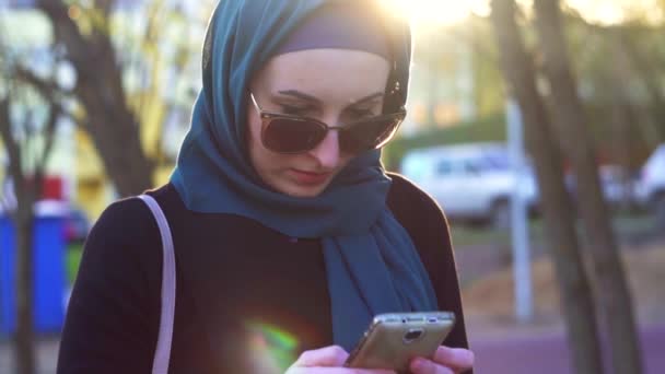 Hijab kız portresi telefon günbatımında parkta kullanır — Stok video