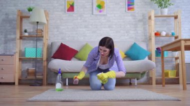 Hoşnutsuz eldiven giymiş genç bir kadın halıyı elleriyle temizliyor.