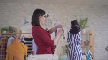Kumaşla çalışan, gözlüklü, genç ve güzel bir kadın moda tasarımcısı.