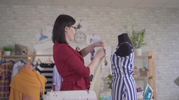 Kumaşla çalışan, gözlüklü, genç ve güzel bir kadın moda tasarımcısı. — Stok video