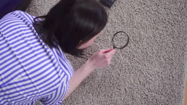 年轻女子用放大镜检查地毯，从顶上看 — 图库视频影像
