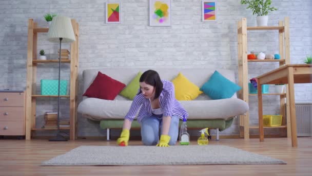 Joven mujer en guantes está feliz de limpiar la alfombra con sus manos — Vídeo de stock