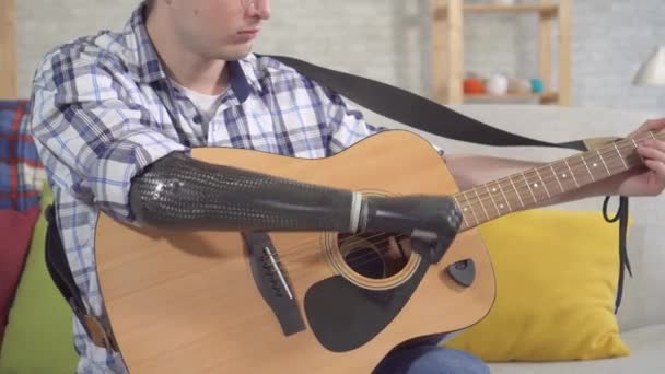 Ung man med en bionisk protes arm spelar en gitarr — Stockvideo