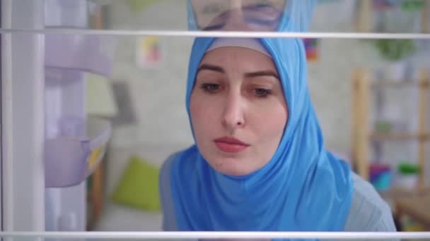 Jonge moslimvrouw in een nationale hoofddoek kijkt in de lege koelkast — Stockvideo