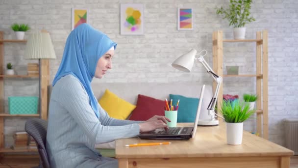 Fiatal muszlim nő egy nemzeti fejkendőben ül egy laptopnál — Stock videók