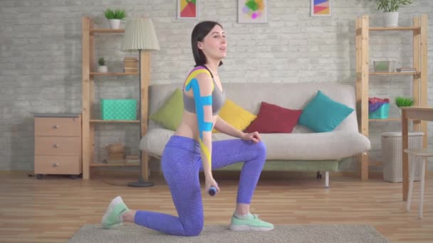 Female athletes with a kinesiotape is engaged with dumbbells at home — Stock Video