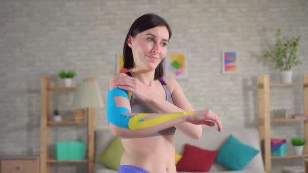 Portrait beautiful young female athlete posing colorful Kinesiotape on hand — Stock Video