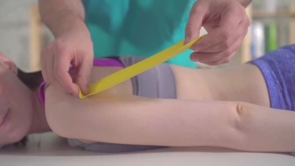 Handen fysiotherapeut in uniform stokken op de huid een speciale kinesio tape gebruikt bij sportblessures — Stockvideo