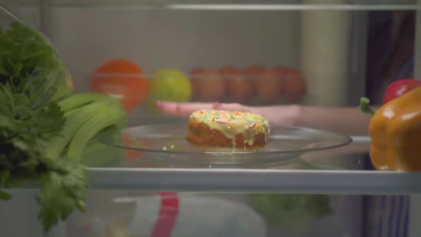 Нарушение диеты, ночной голод, рука в холодильнике берет пончик — стоковое видео