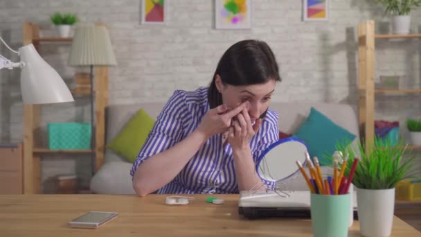Молода жінка одягає контактні лінзи, сидячи за столом — стокове відео