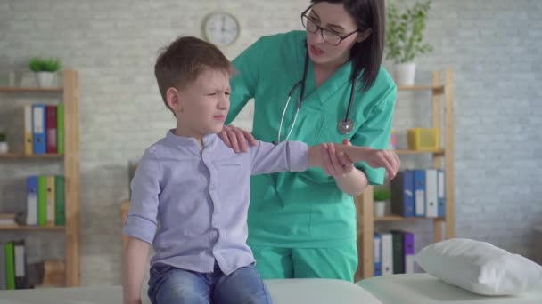 Маленький мальчик с болью в руке на приеме у физиотерапевта — стоковое видео