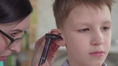 Bir otolarolog, küçük bir çocuğun kulaklarını yakından inceliyor.