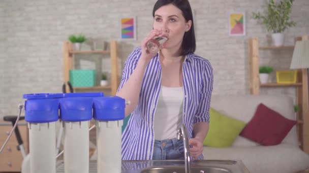 Молода жінка з здивуванням п'є воду з-під фільтра — стокове відео