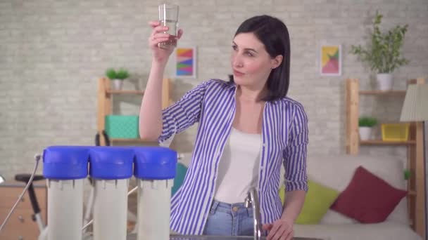 Молодая женщина с удовольствием пьет фильтрованную воду из крана — стоковое видео