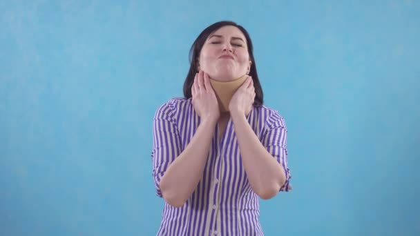 Mujer joven con cuello protector contra el dolor de cuello de pie sobre fondo azul — Vídeos de Stock