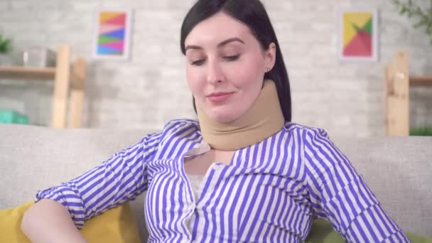 Молодая женщина сидит на диване с воротником на шее и использует ноутбук крупным планом — стоковое видео