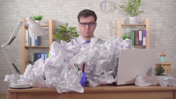 Unruffled young man office worker is talking on the phone with a heaps of papers on the office desk — Stock Video