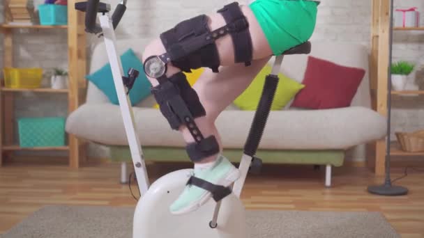 Young woman knee bend orthosis knee brace after injury on a stationary bike knee bend orthosis knee brace after injury — Stock Video