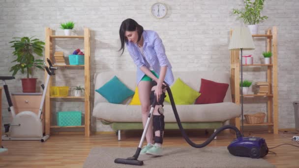 Hospodyňky po zranění koleno ohýbat ortézu koleno podprsenka vysavače v obývacím pokoji — Stock video