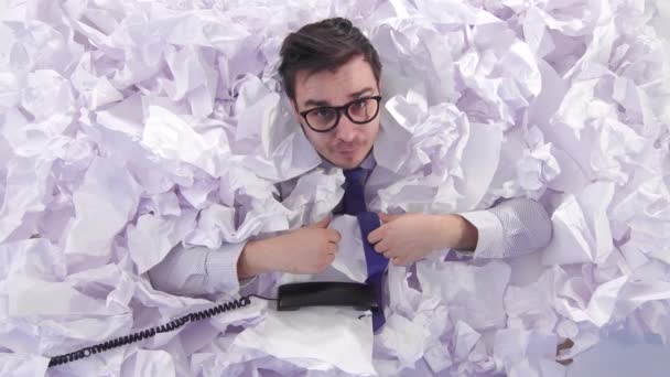 Travailleur de bureau masculin positif avec des lunettes donne un pouce vers le haut et regarde la caméra dans un grand tas de papier froissé — Video