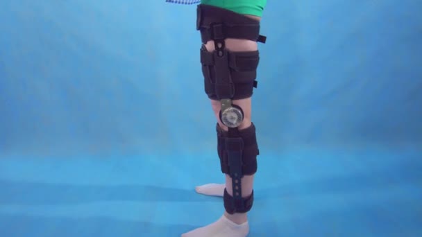 A young woman squatting after injury knee bend orthosis knee brace blue background — 비디오