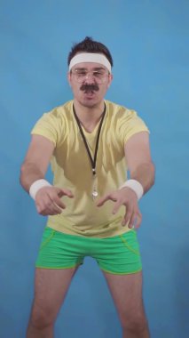 Seksenlerin tarzında bıyıklı antrenör, antrenmanı motive eder ve poz verir.
