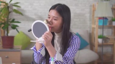 a Portrait of an Asian young woman using makeup in the living room close up
