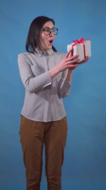 happy young business woman with a gift box in her hands stands on a blue background vertical video