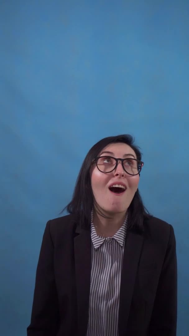 Positive young business woman in a suit stands on a blue background of a vertical video — Stockvideo