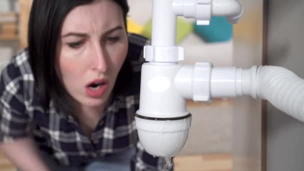 Jonge vrouw in een shirt ontdekte een lek onder de gootsteen en belt de loodgieter — Stockvideo