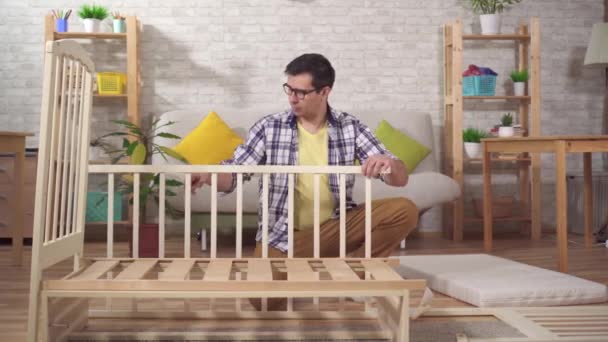Pozitív fiatal férfi jövendőbeli apa gyűjt egy gyermek ágy a hálószobában — Stock videók