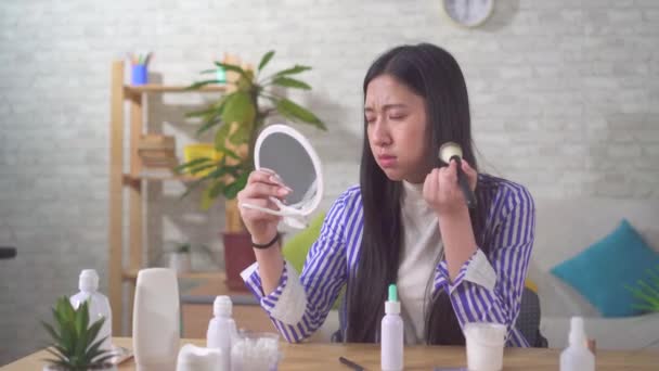 Portrait of a disgruntled Asian young woman using makeup in the living room — 图库视频影像