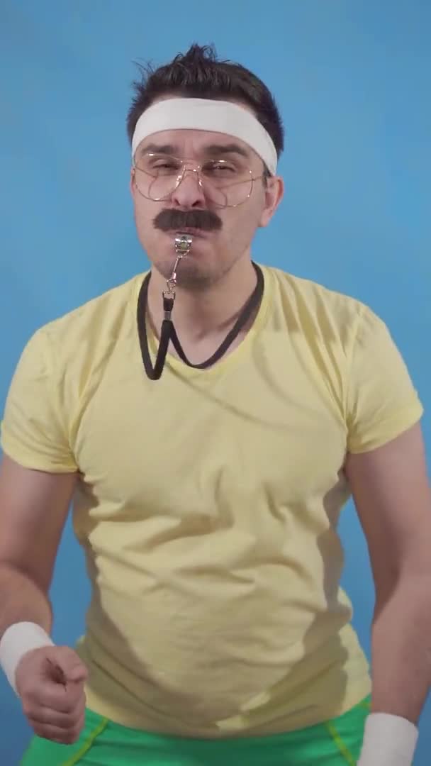 Engraçado treinador aberração com um bigode no estilo de 80 usa um apito em um fundo azul — Vídeo de Stock