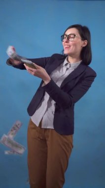 young business woman scatters throws paper money on a blue background of a vertical video