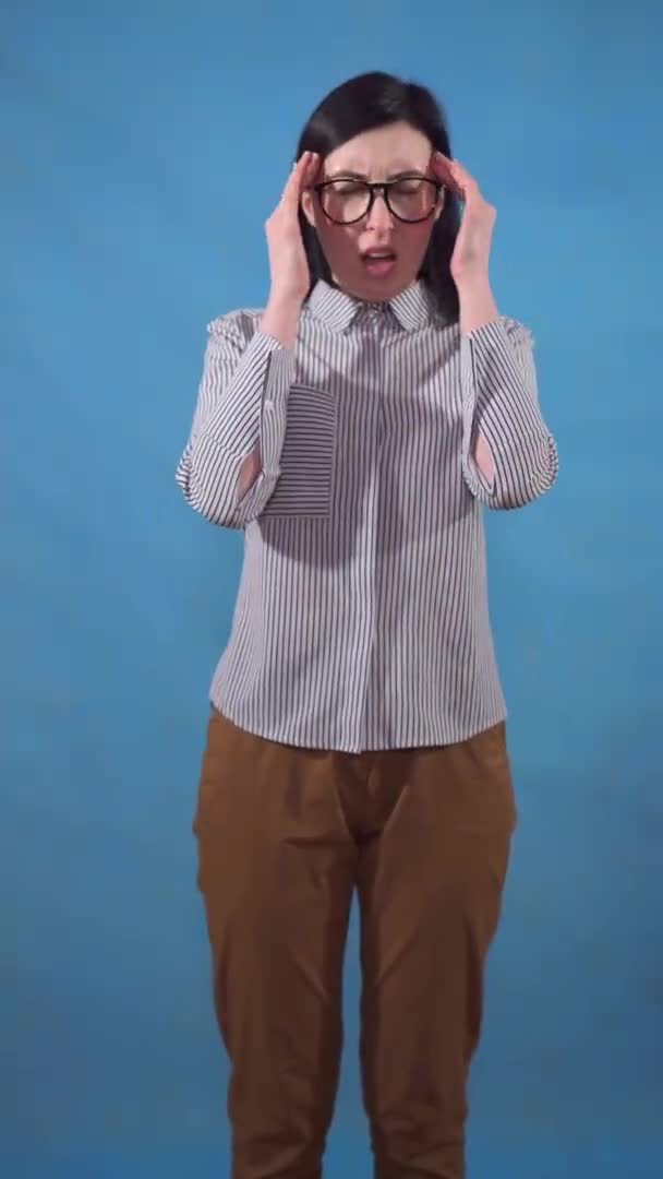 Young business woman experiences a headache standing on a blue background vertical video — ストック動画