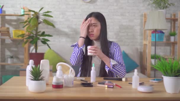 Una joven hermosa mujer asiática utiliza crema facial sentado en la mesa en casa — Vídeos de Stock