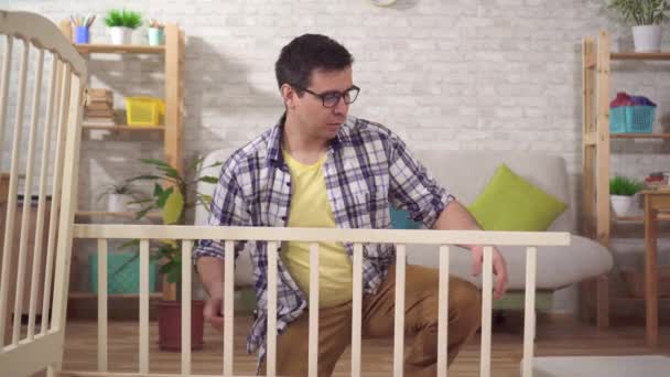 Portret positieve jongeman toekomstige vader verzamelt een bed in de slaapkamer — Stockvideo