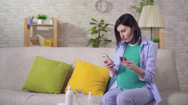 Озадаченная молодая беременная женщина с таблетками в руках ищет в Интернете — стоковое видео