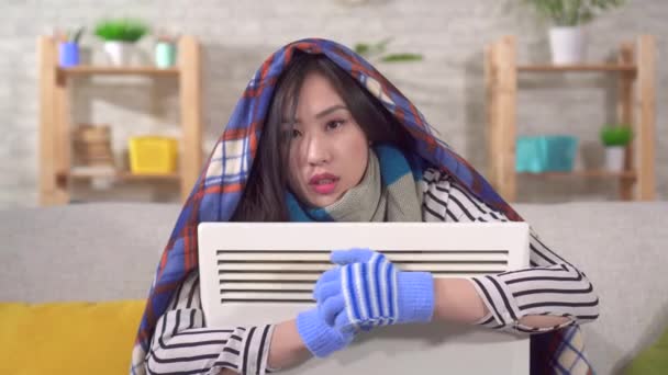 Retrato de una joven asiática congelada sentada con un calentador en el salón — Vídeos de Stock