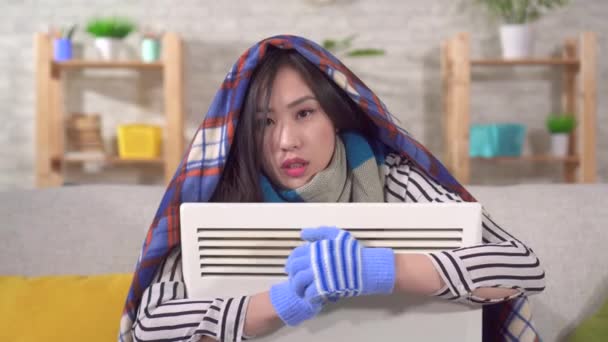 Portrait of a freezing young asian woman sitting with a heater in the living room — Stock videók