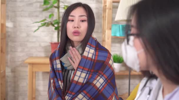 Sick asian woman in a plaid and gloves with a temperature communicates with the doctor — Stockvideo