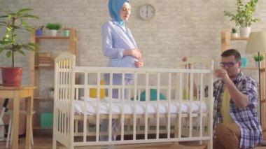 happy Muslim family and pregnant young woman in hijab collects baby bed
