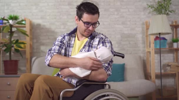 Um jovem pai é um homem deficiente em uma cadeira de rodas com um recém-nascido em suas mãos — Vídeo de Stock
