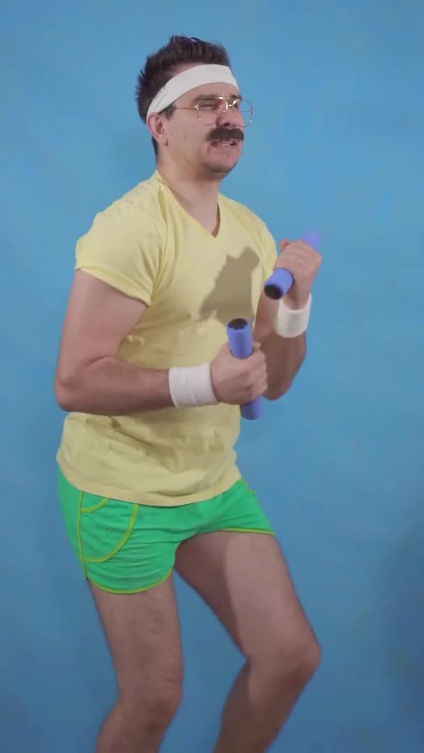 Funny mustachioed man in the style of the 80s with dumbbells doing sports on a blue background vertical video slow mo — Stock Video