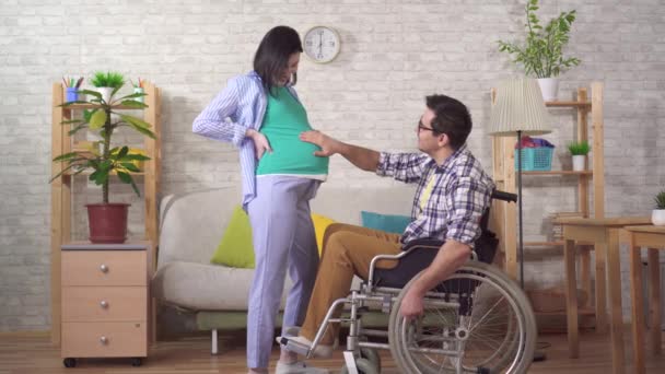 Инвалид в инвалидном кресле и его беременная жена будущие родители — стоковое видео