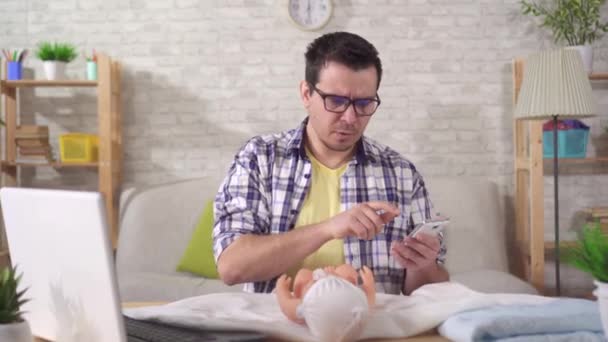 Young father-to-be has problems with learning, swaddling a baby doll and looking at the camera — 图库视频影像